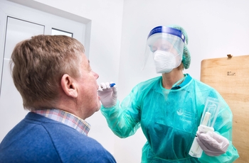 Ärztin nimmt in Sicherheitskleidung Rachenabstrich bei Patient