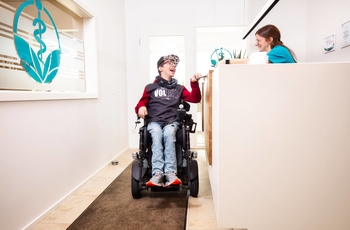 Inklusion eines Jungen im Rollstuhl in der Arztpraxis HVM mit Arztpersonal am Empfang
